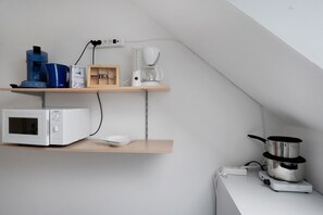 Een keuken met een magnetron, koffiezetapparaat en waterkoker op een plank, en een pan op een fornuis.