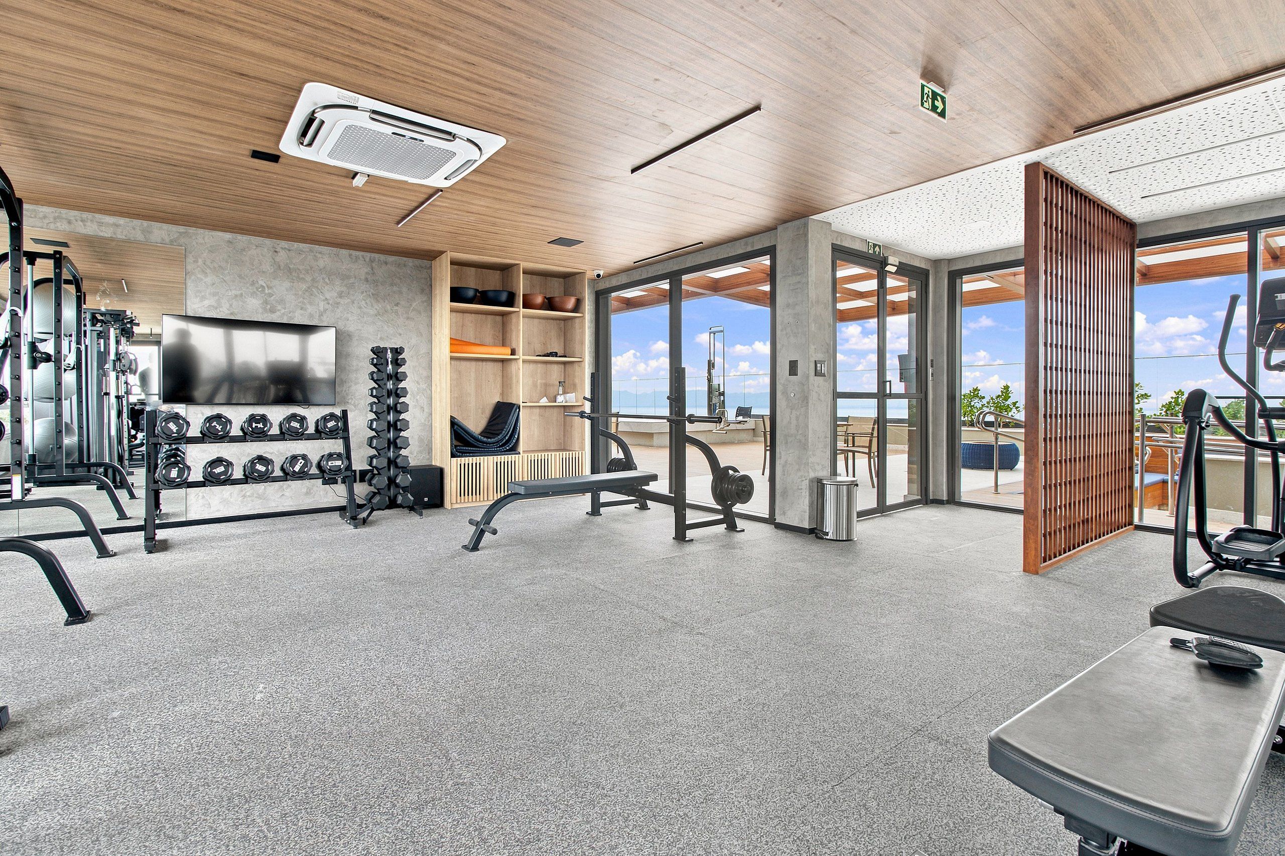 Une salle de sport moderne équipée de divers appareils d’exercice, d’un téléviseur et offrant une vue sur l’extérieur grâce à de grandes portes vitrées.