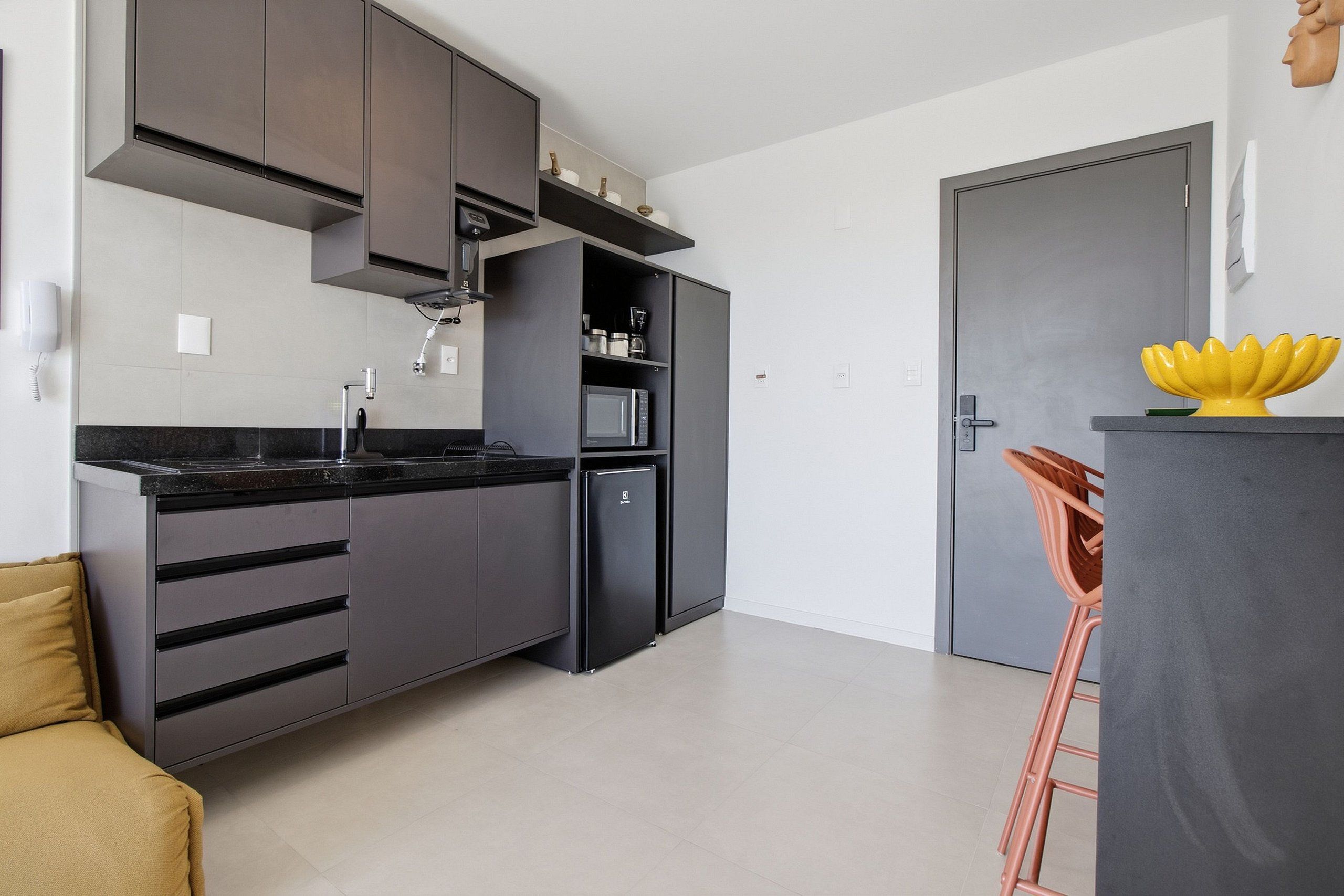 Une cuisine moderne avec des meubles de rangement aux couleurs sombres, un four à micro-ondes encastré et une machine à café.
