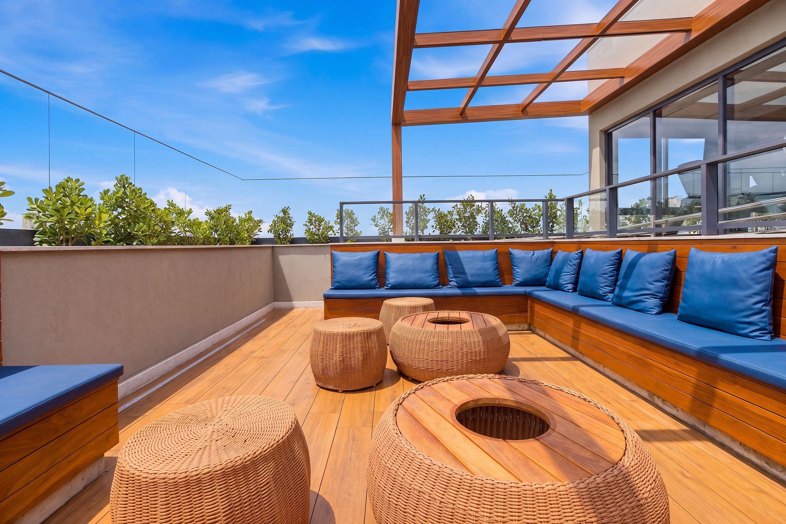 Une terrasse sur le toit avec une plateforme en bois, des sièges rembourrés bleus et des poufs en osier.
