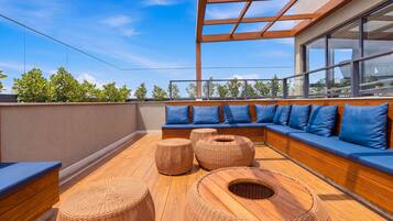 Une terrasse sur le toit avec une plateforme en bois, des sièges rembourrés bleus et des poufs en osier.