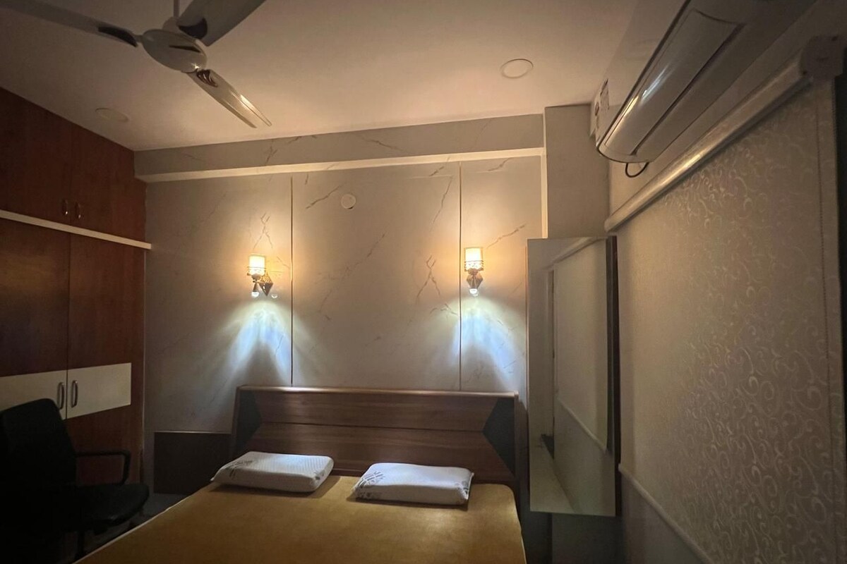Una habitación de hotel con una cama, dos lámparas de noche, un ventilador de techo y un equipo de aire acondicionado.