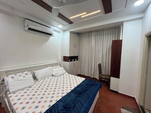 A hotel room with a bed, an air conditioning unit, a wardrobe, a chair, and a window with curtains.