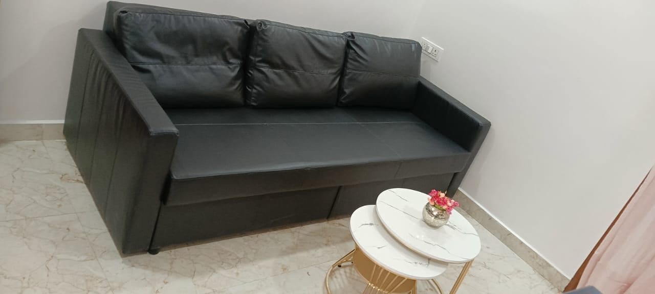 A dark-colored sofa against a wall, a small round table with a vase, and a marble floor.