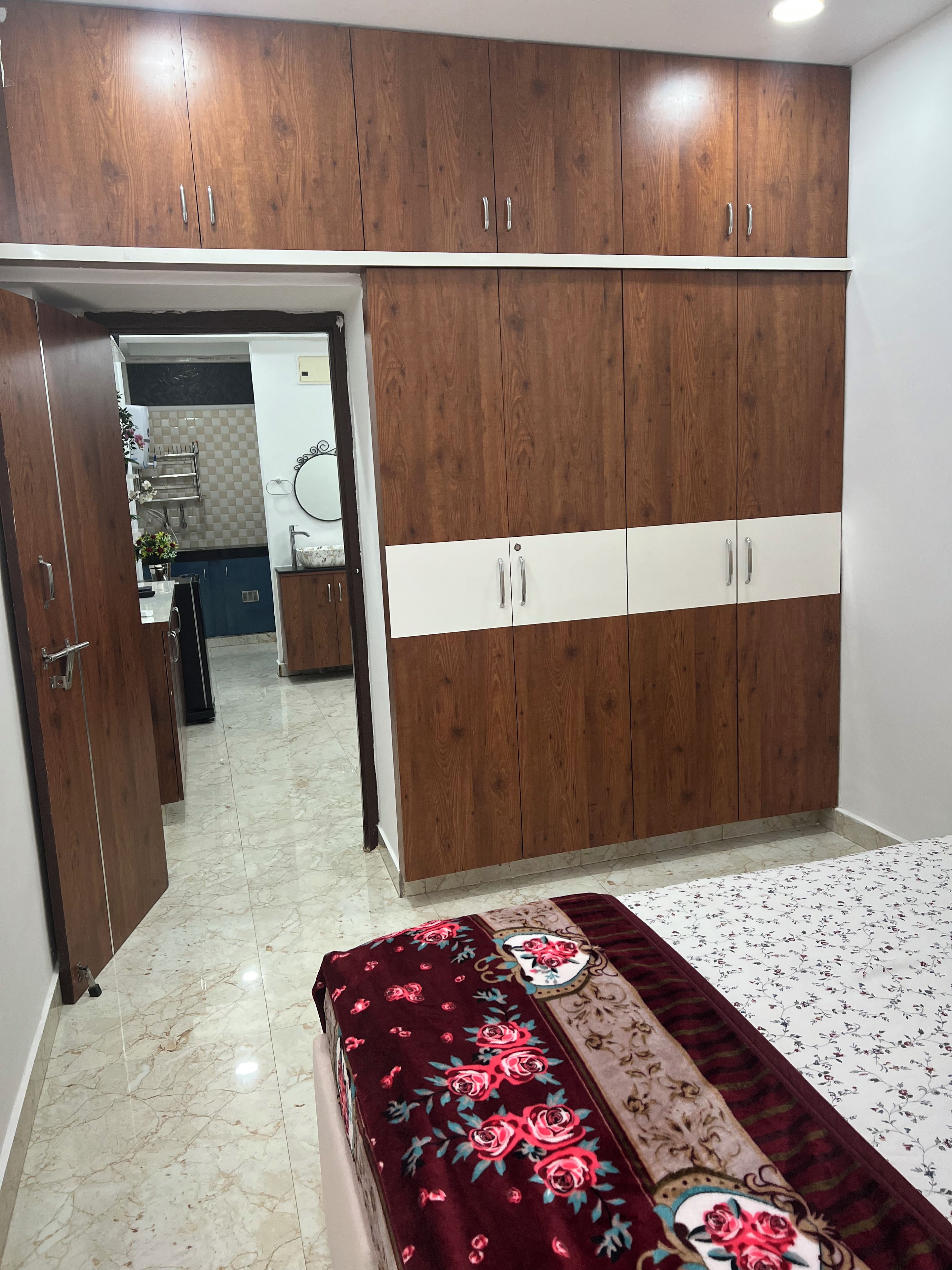 Un dormitorio con un armario grande, una cama con cubrecama floral y un baño visible a través de una puerta abierta.