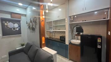 Una cocina moderna con armarios oscuros, un refrigerador negro y un microondas. Hay una zona de comedor con un sofá gris y una mesita.