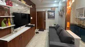 Ein modernes Wohnzimmer mit Fernseher, Holzschränken, einem grauen Sofa und einem Deckenventilator.