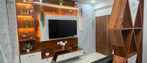 Un salon moderne doté d’un téléviseur à écran plat, d’étagères en bois et de plantes décoratives.