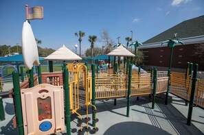 Ein Spielplatz mit verschiedenen Spielgeräten, darunter ein Kletterbereich und eine Rutsche, umgeben von Sicherheitsgeländern.