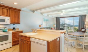 A kitchen with wooden cabinets, a microwave, a kettle, and a dishwasher. - 235 The Vue  -- New Listing (Tybee Island)