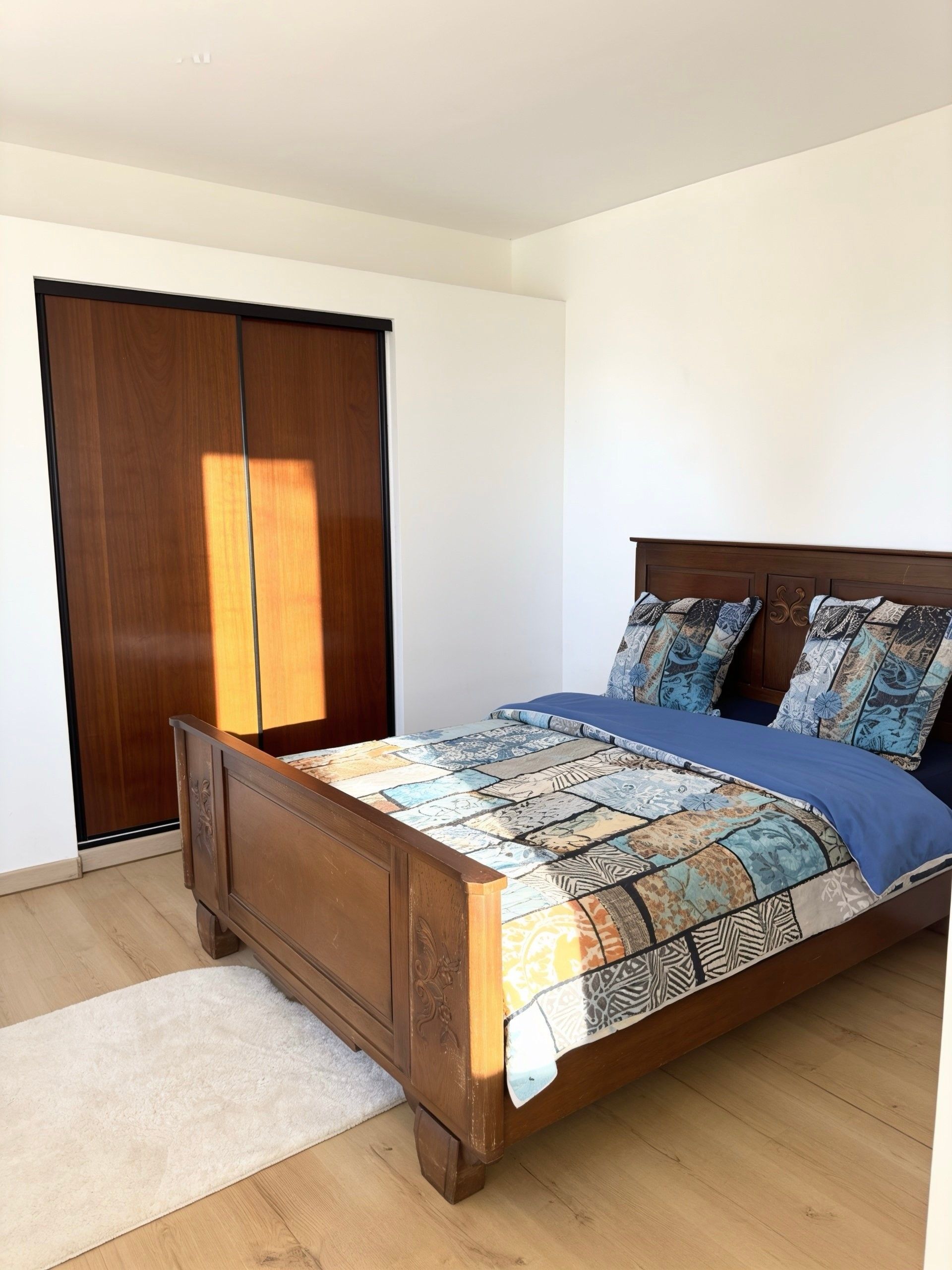 A bedroom with a wooden bed, patterned bedding, and a white rug.