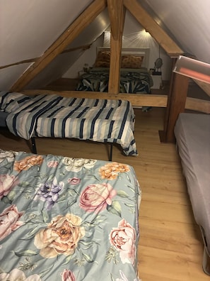 A dormitory room with two beds, wooden beams, a window, and a bedside table.