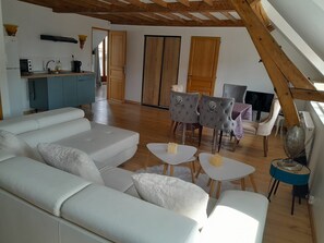 Ein modernes Wohnzimmer mit einer Couch, zwei Sesseln, einem Couchtisch und einem Essbereich mit Stühlen und einem Tisch.