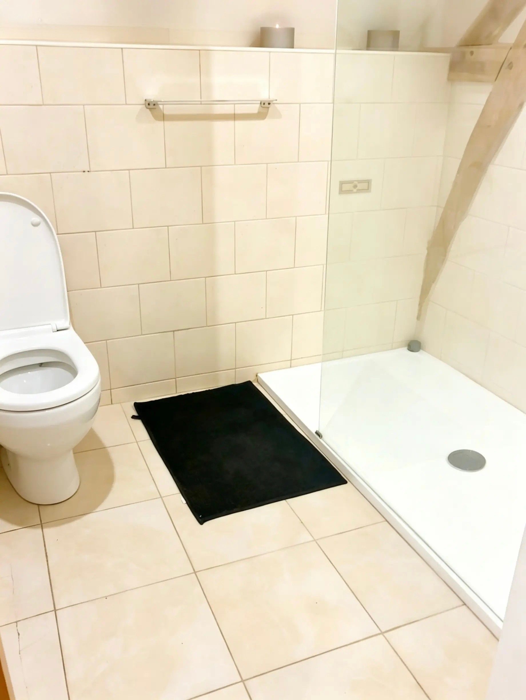 A bathroom with a toilet, a black mat, and a glass shower enclosure.
