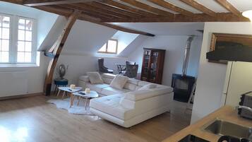 Una sala de estar estilo loft con un sofá blanco, vigas de madera, chimenea y tragaluces.