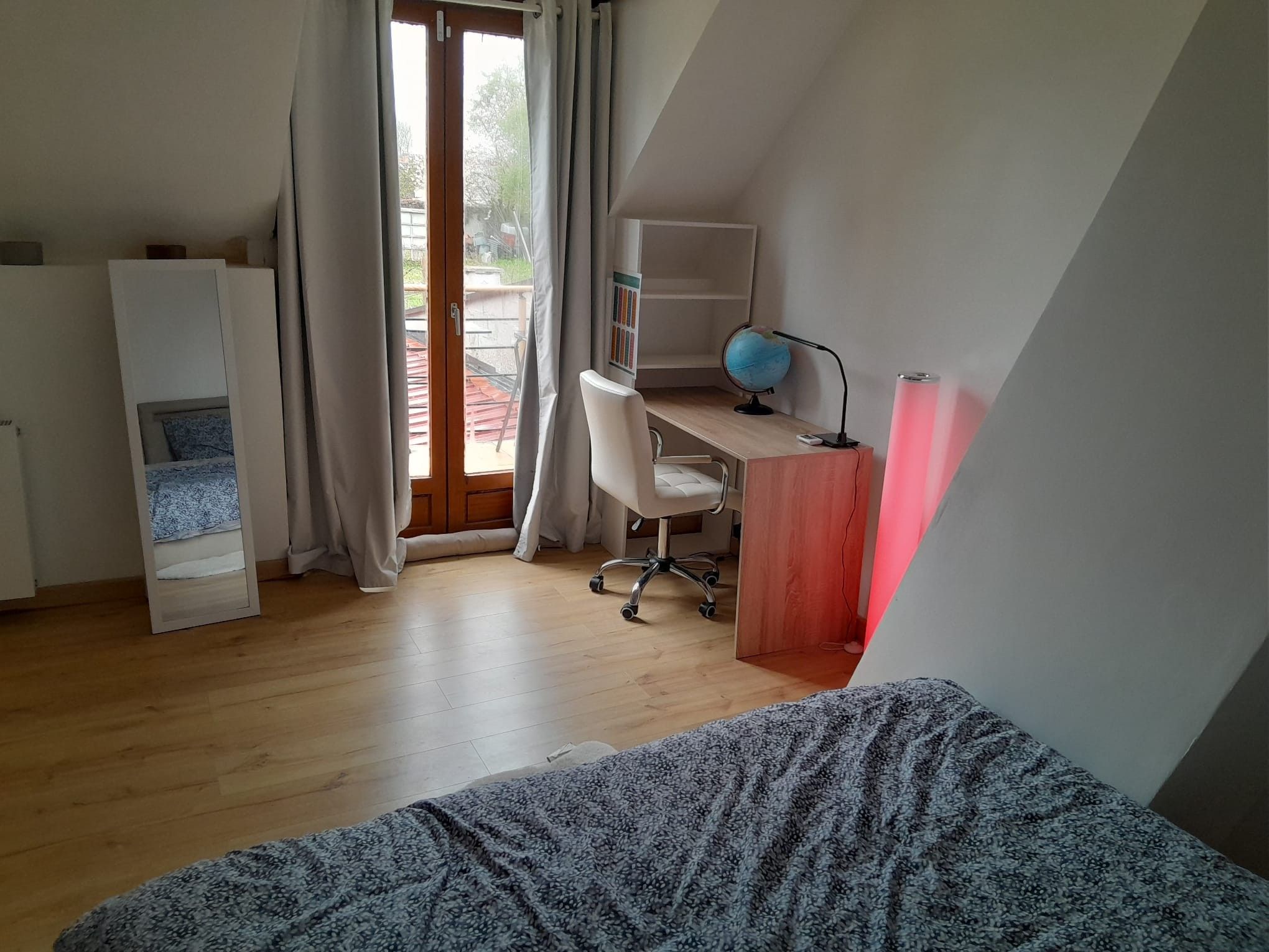 A room with a bed, a desk with a globe and lamp, and a view through a window.