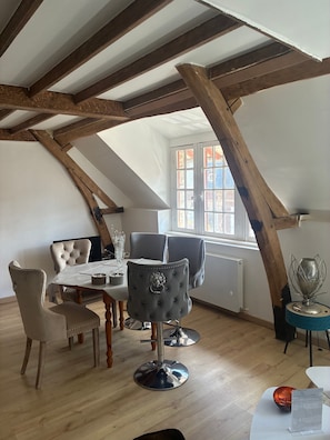 A dining area with a high ceiling, exposed wooden beams, a table with chairs, and a window with a view.