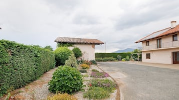 Una zona residenziale con vialetto lastricato, un piccolo edificio bianco con tetto in tegole e una casa più grande con balcone.