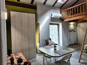 A room with a lofted wooden staircase, a dining table with chairs, a window with curtains, and a hanging coat rack. - Studio at Agriturismo al Campo del Nocciolo in the countryside with Maira Valley view (Busca)
