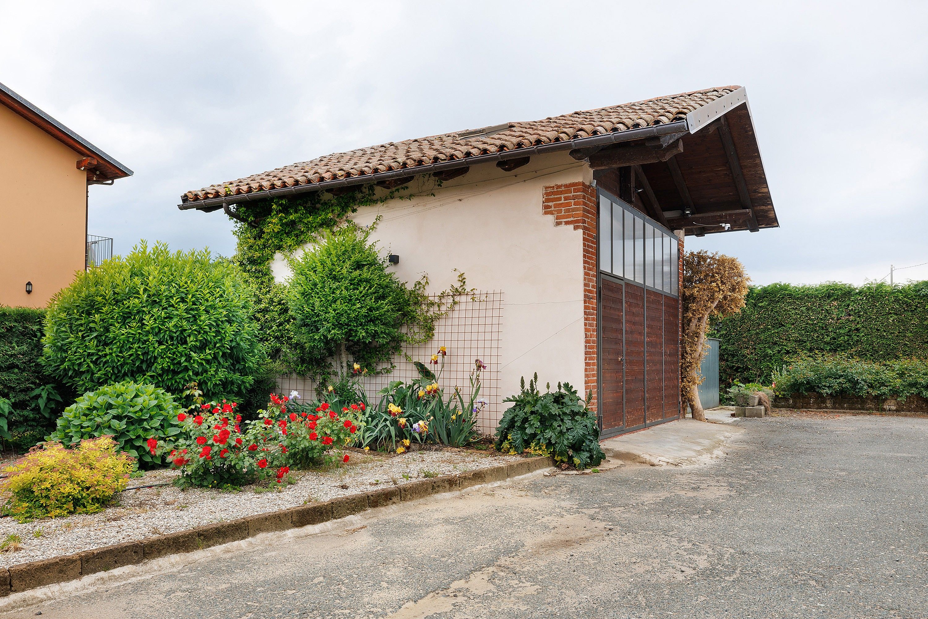 Un edificio residenziale con tetto in tegole, una sezione in mattoni e un giardino con diverse piante e fiori.