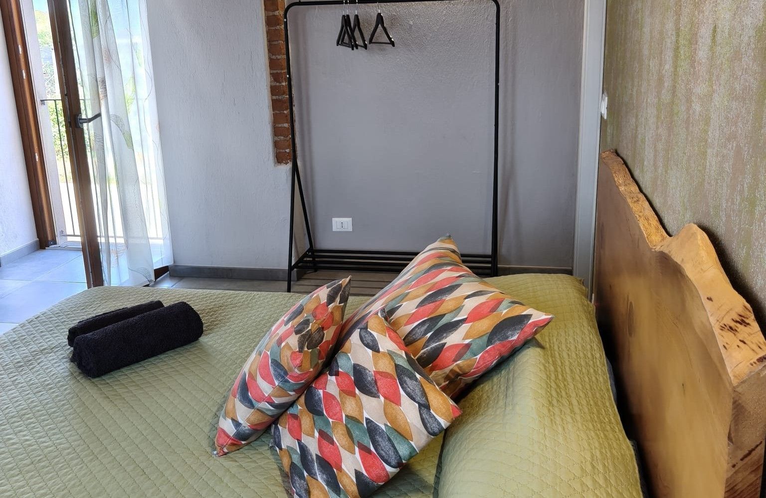 A bedroom with a bed, pillows, a wooden headboard, and a window with curtains.