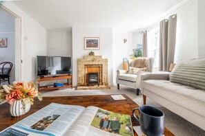 A living room with a fireplace, a sofa, a television, and a coffee table with a book and a mug. - Swift Host | Furtherfield | Sleeps 3 | Countryside | Garden (Reedham)