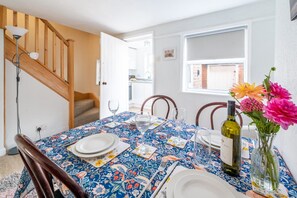 A dining area with a table set for two, a bottle of wine, and a vase with flowers. - Swift Host | Furtherfield | Sleeps 3 | Countryside | Garden (Reedham)