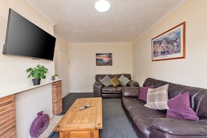 A living room with a flat-screen TV, a leather sofa, a wooden coffee table, and a painting on the wall. - Bhllys (Wolverhampton)