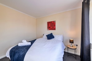 Ein Hotelzimmer mit Bett, einem Wandbild, einer Nachttischlampe und einem gefalteten Handtuch.