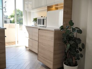 A modern kitchen with wooden cabinets, a microwave, and a potted plant. - Apartment Suite in Cagnes-sur-Mer (Cagnes-sur-Mer)