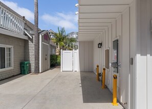 A clean, well-maintained corridor with a white door, a trash bin, and a utility box on the right side. - Brand New Construction | AC | Fire Pit | Garage Parking | Walk to All! (San Diego)