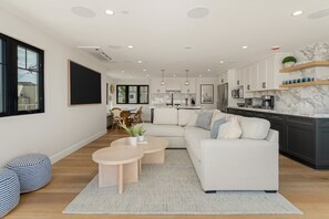 Ein modernes Wohnzimmer mit Sofa, Couchtisch und Essbereich, im Hintergrund eine Küche.