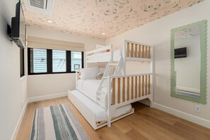 A room with bunk beds, a television, a window with blinds, and a patterned ceiling. - Brand New Construction | AC | Fire Pit | Garage Parking | Walk to All! (San Diego)