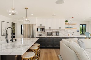 A modern kitchen with a marble countertop, stainless steel appliances, and a central island with bar stools. - Brand New Construction | AC | Fire Pit | Garage Parking | Walk to All! (San Diego)