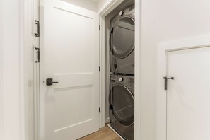 A laundry room with two stacked washing machines and a white door. - Brand New Construction | AC | Fire Pit | Garage Parking | Walk to All! (San Diego)