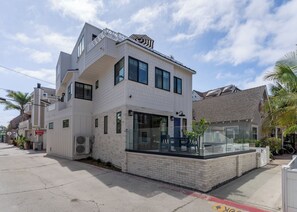 A modern two-story residential building with a balcony, large windows, and a visible garage door. - Brand New Construction | AC | Fire Pit | Garage Parking | Walk to All! (San Diego)