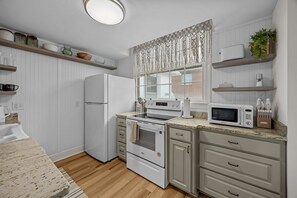 A kitchen with a refrigerator, oven, microwave, and a window with patterned curtains. - Waterfront Porch Escape (New Bern)