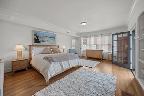 A bedroom with a bed, bedside tables, a dresser, a window with curtains, and a door. - Waterfront Porch Escape (New Bern)