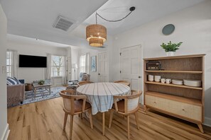 A modern living room with a dining area, wooden flooring, a television, and a bookshelf. - Waterfront Porch Escape (New Bern)