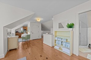 A spacious room with a wooden floor, a white door, and a shelf with folded towels. - Downtown Riverfront Retreat (New Bern)