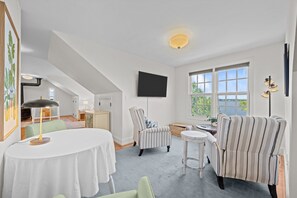 A modern living room with a flat-screen TV, striped armchairs, a round table, and a view of a lake through large windows. - Downtown Riverfront Retreat (New Bern)
