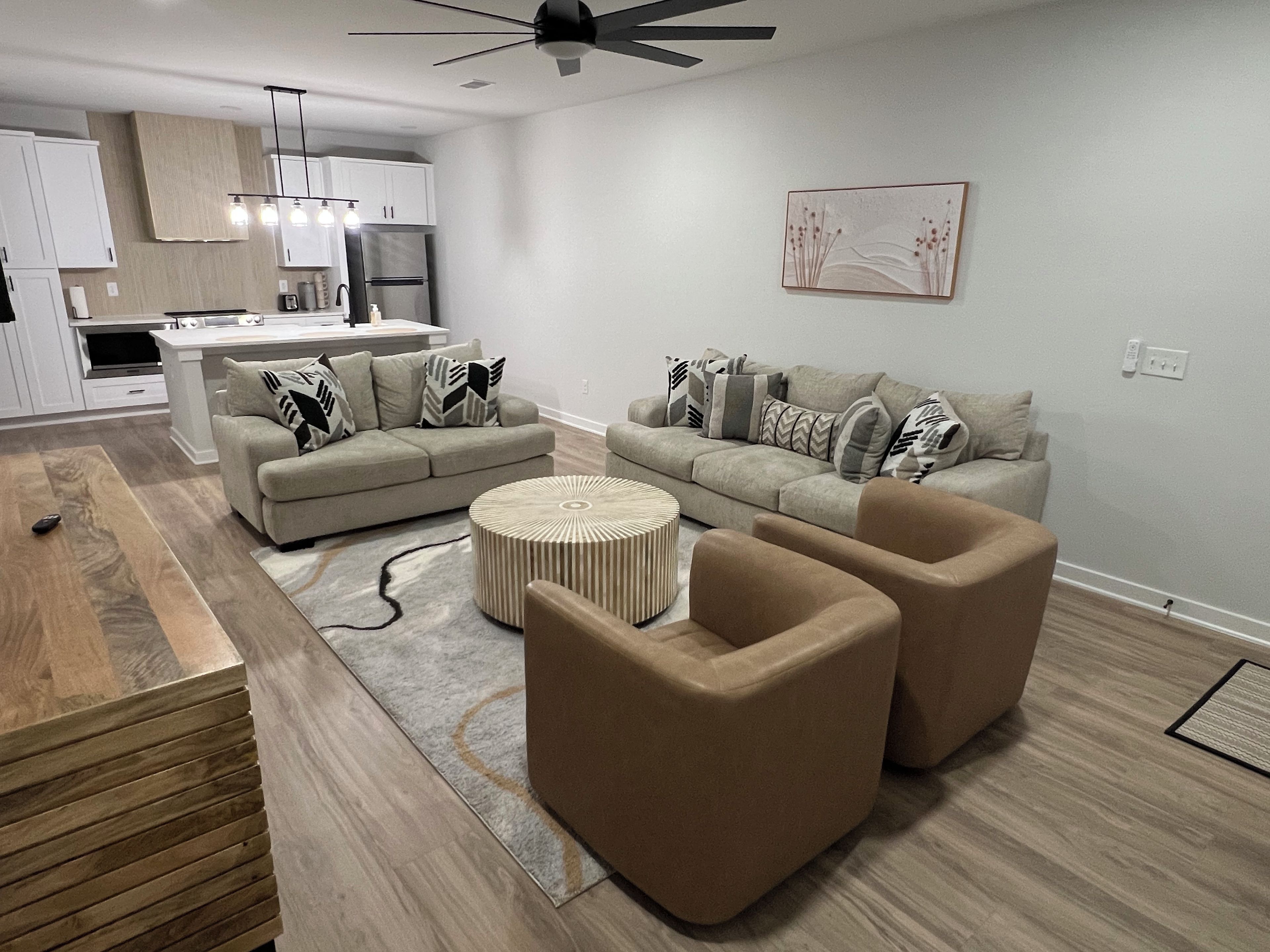 A modern living room with a sectional sofa, a round coffee table, and a kitchen area in the background.