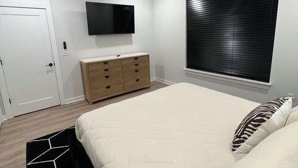 Een slaapkamer met een bed, een plafondventilator, een televisie, een raam met jaloezieën en een dressoir.