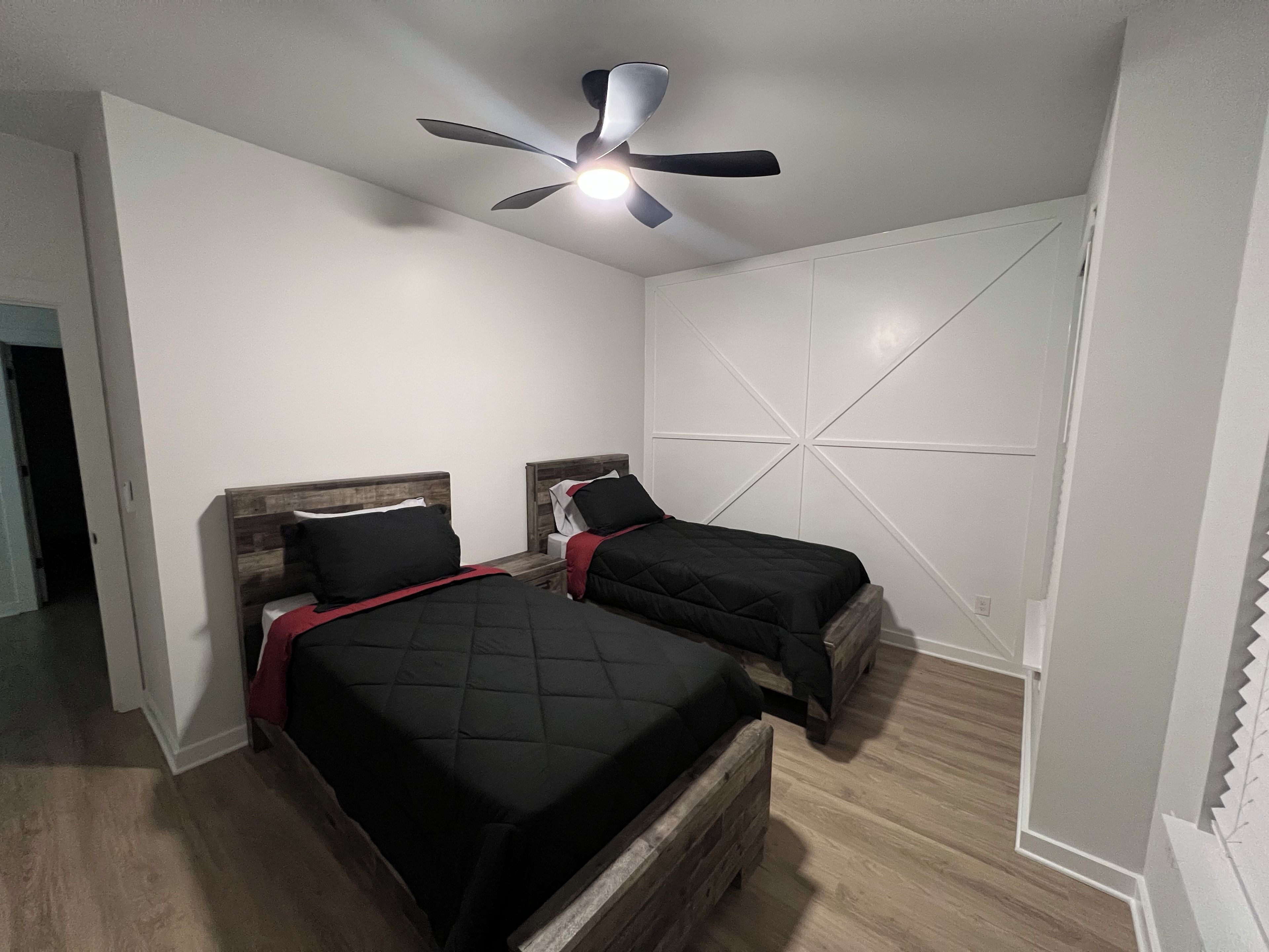 A bedroom with two beds, a ceiling fan, and a white wall with a geometric design.