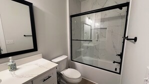 Een badkamer met een toilet, een douchecabine, een betegelde muur van marmer en een wit wastafel met een spiegel erboven.