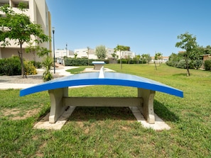 A concrete bench with a blue top in a grassy area with buildings in the background. - Seaside Apartment With Pool (Sérignan)