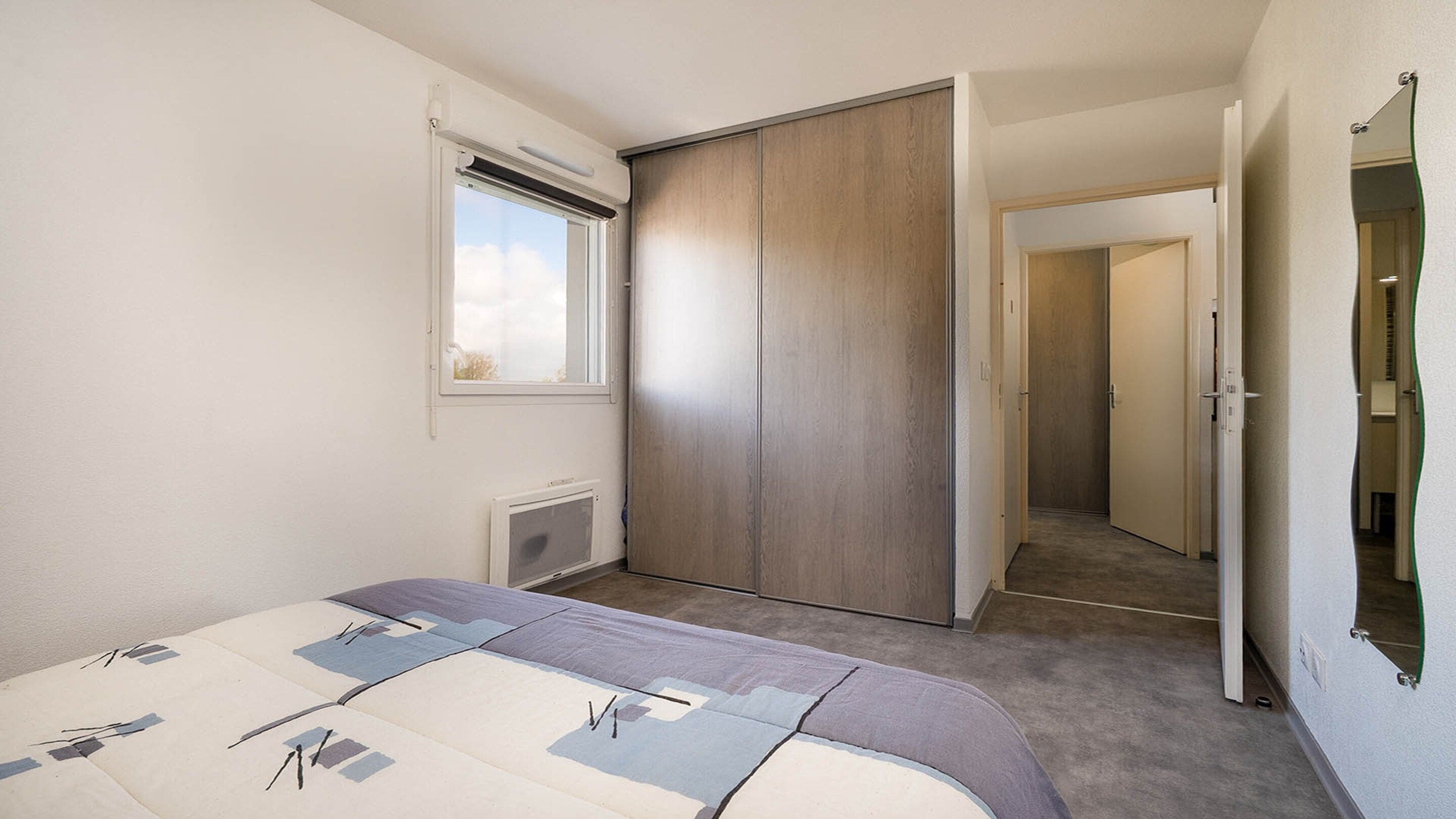 A bedroom with a bed, a wardrobe, a radiator, and a window.