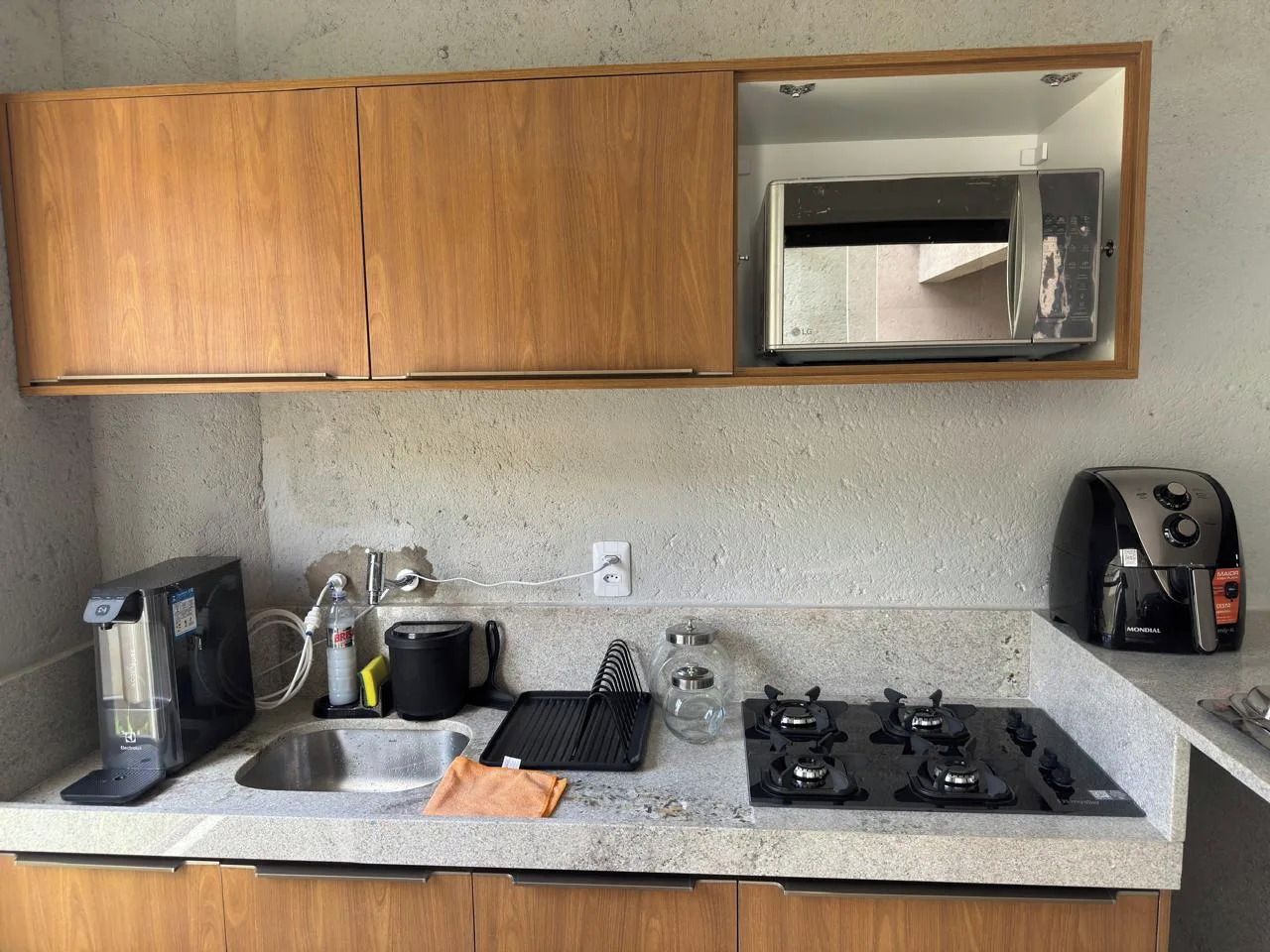 Uma cozinha compacta com micro-ondas integrado, cafeteira, chaleira e fogão a gás.