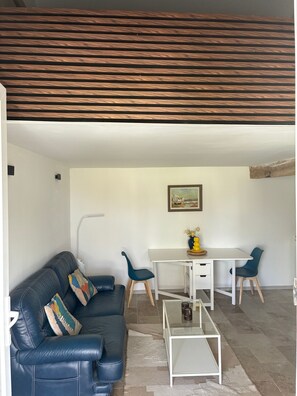 A modern living room with a leather sofa, a dining table with chairs, and a white ceiling with wooden beams.