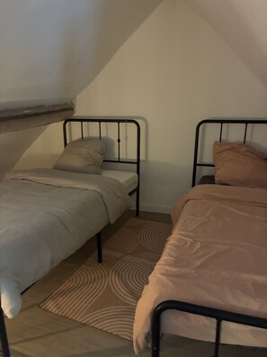 A room with two single beds, each with a mattress and pillow, and a patterned rug on the floor.